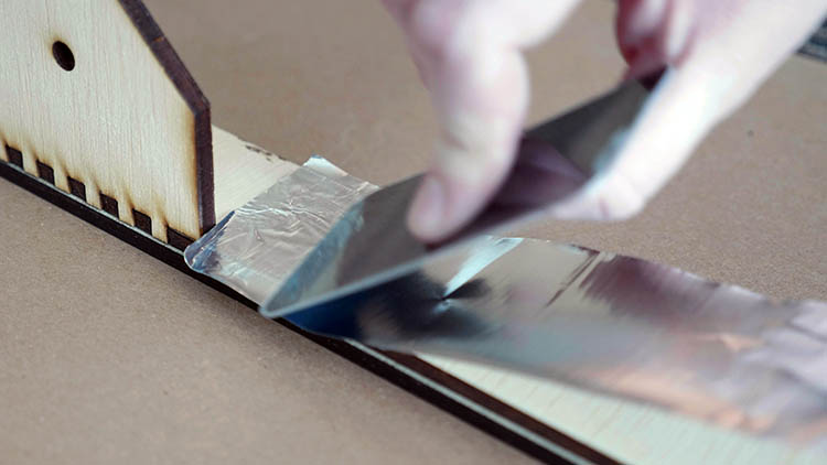 Memasang lakban aluminium ke bagian dalam sisi kotak yang dipotong dengan laser.