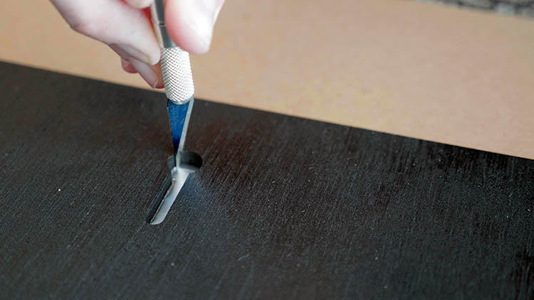 Using an X-ACTO knife to cut the foil tape away from a keyhole slot.