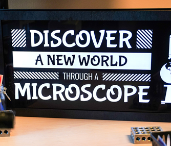 Færdigt LED-belyst skilt på et skrivebord bag et mikroskop.
