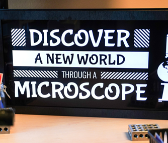 Finished LED-lit sign on a desk behind a microscope.